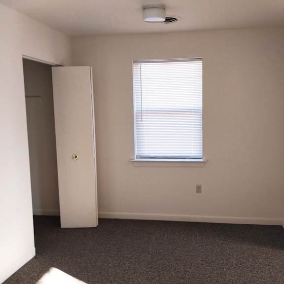 a room with a white door, a window with blinds, and a carpeted floor.