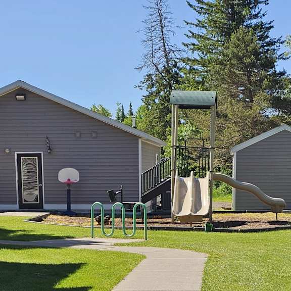 a playground with a slide, swings, and a picnic table is located in front of a building.