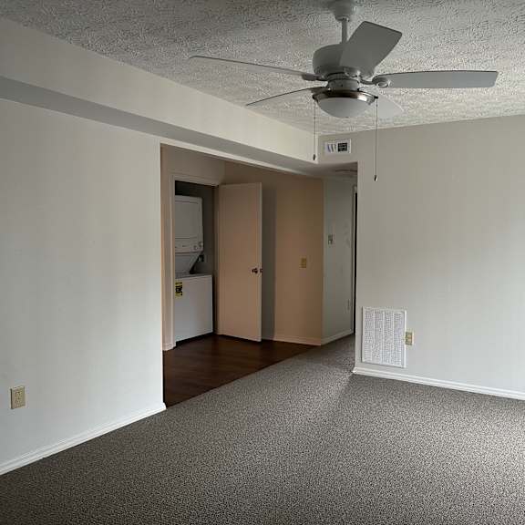 an empty living room with a ceiling fan and white walls