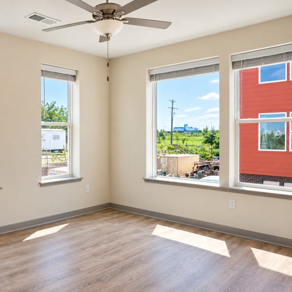 a room with a ceiling fan and three windows.