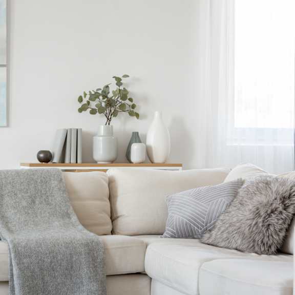 a white couch with grey pillows and a grey blanket.