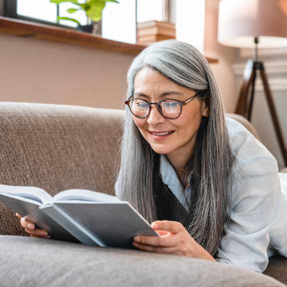 a person is reading a book on a grey couch.