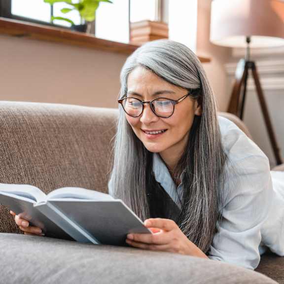 a person is reading a book on a grey couch.