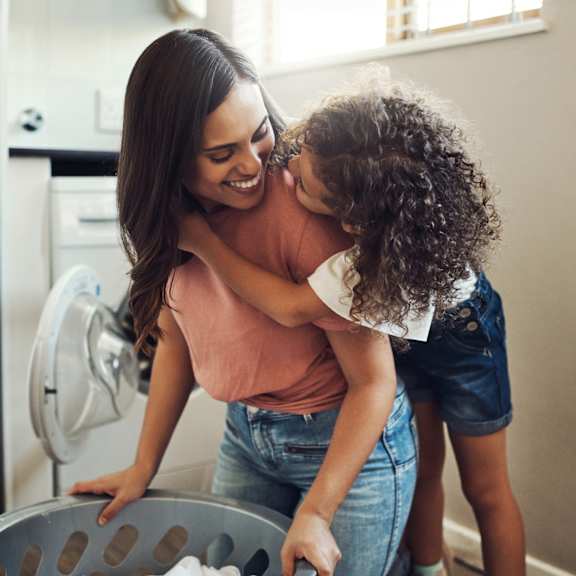 a woman and a child are standing in a kitchen, with the woman holding the child up to look into an open refrigerator.