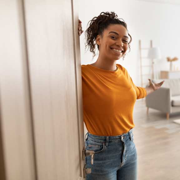a woman in a yellow top and blue jeans stands in a room with a couch and a rug.