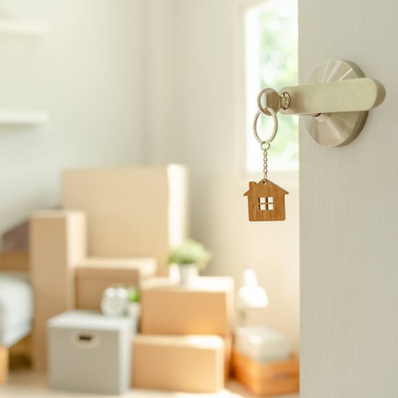 a key hanging from a door handle with boxes and a plant in the background.