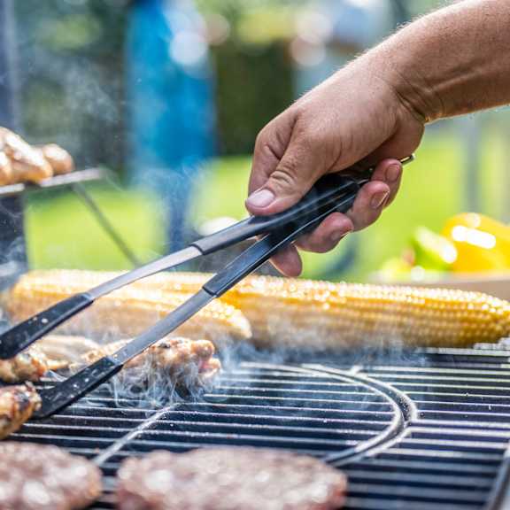 a person is grilling corn and meat on a barbecue.