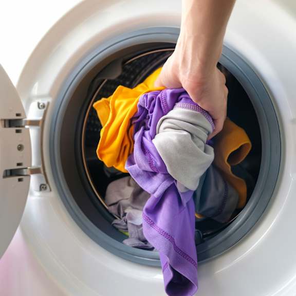 a person is loading clothes into a washing machine.