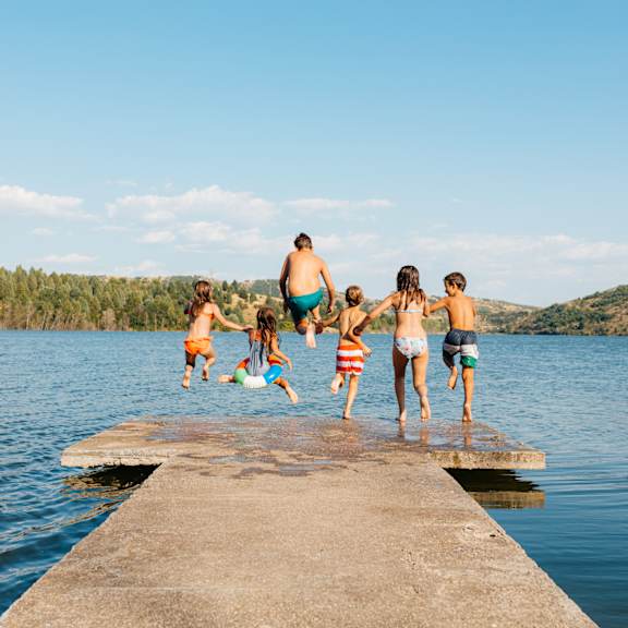 a group of people jumping into a lake from a concrete pier.