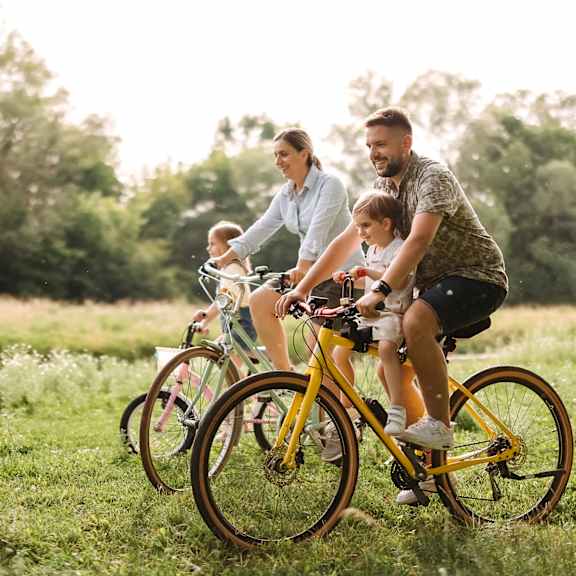 a family of three is riding a yellow bicycle in a field.