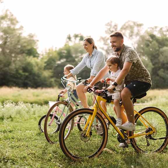 a family of three is riding a yellow bicycle in a field.