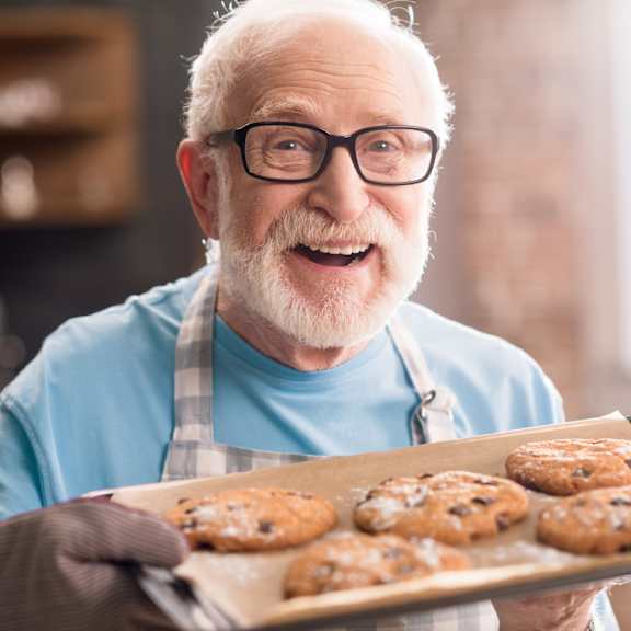 an elderly man with glasses and a beard is holding a tray of freshly baked cookies.