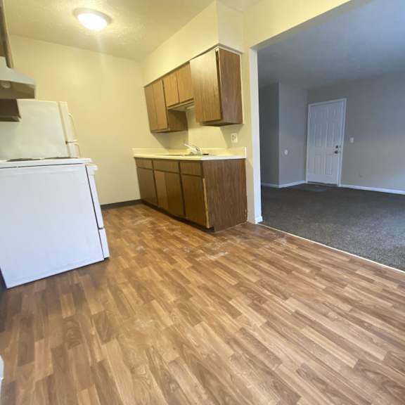 an empty living room with a kitchen and wood flooring