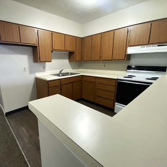 an empty kitchen with white countertops and wooden cabinets