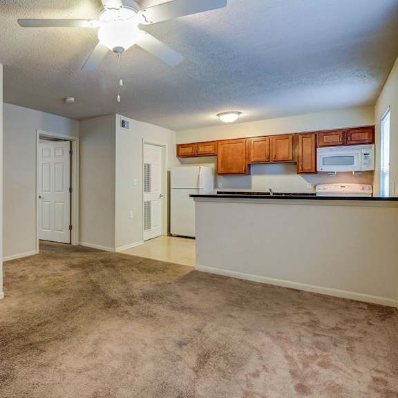 an empty living room with a kitchen and a ceiling fan