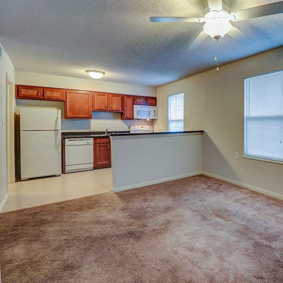 an empty living room with a kitchen and a ceiling fan
