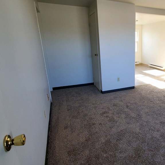 a room with a carpeted floor and white walls and a door to a hallway