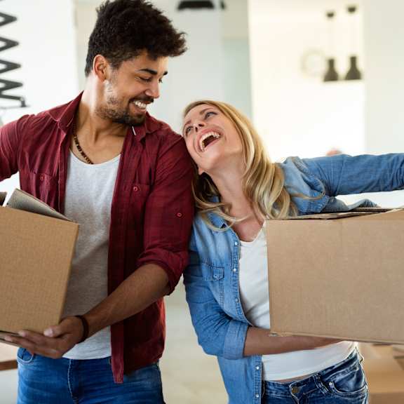 a couple laughing while holding boxes in a room