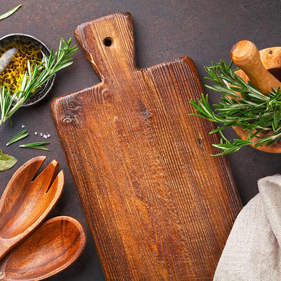a wooden cutting board with a handle is surrounded by various herbs and spices.