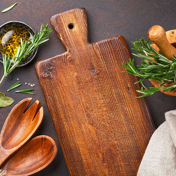 a wooden cutting board with a handle is surrounded by various herbs and spices.