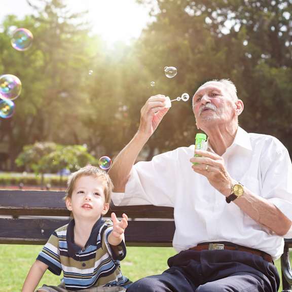 an older man and a child blowing bubbles in a park