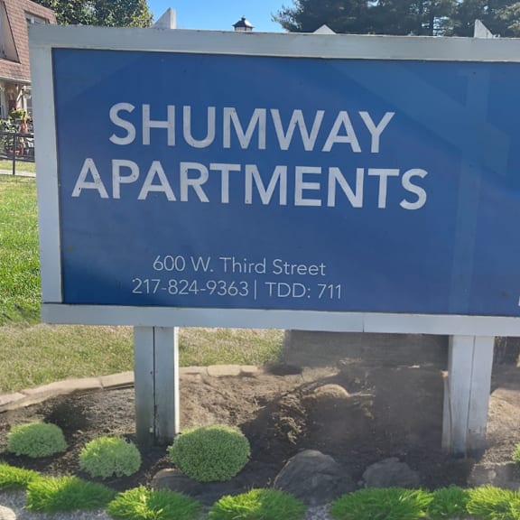 a blue sign that says in front of a yard with plants
