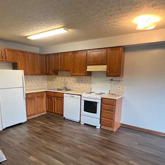 an empty kitchen with wooden floors and white appliances