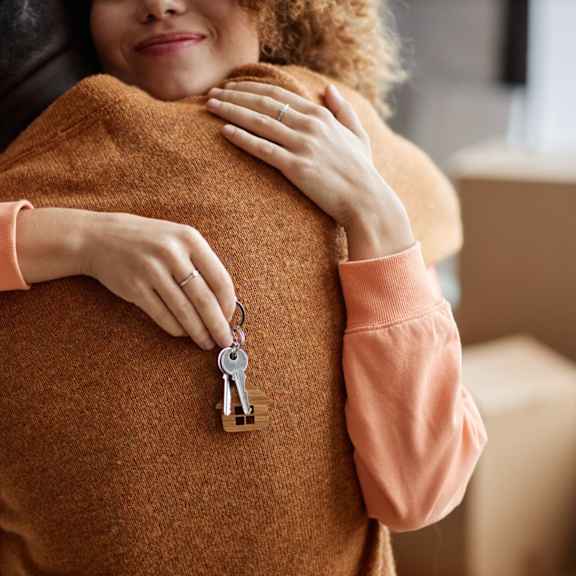 a person in a brown sweater is hugging another person and has a key hanging from their sweater.