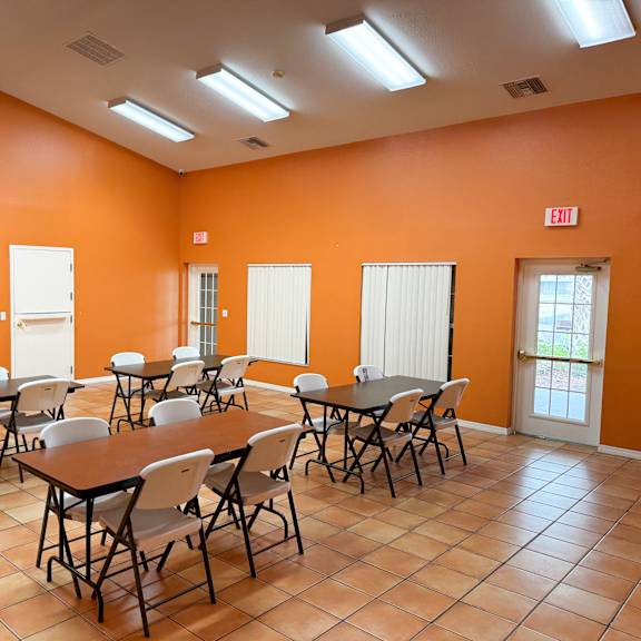 a room with orange walls and tiled floors has tables and chairs set up.