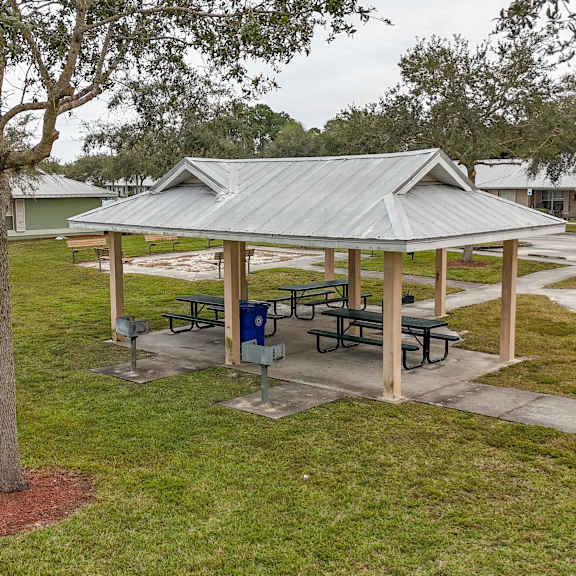 a covered picnic area with benches is surrounded by green grass.