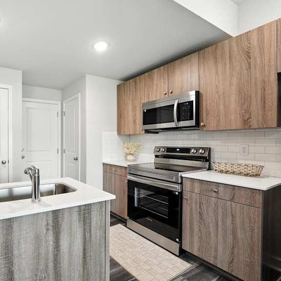 Thumbnail 3 of 23 A modern kitchen with a sink, oven, and microwave.