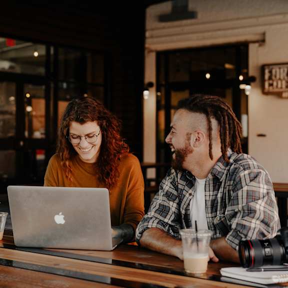 Two people sitting at a table with a laptop and a camera.