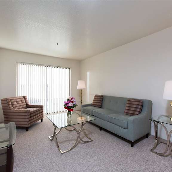 a modern living room here at outlook apartments with a gray sofa, striped armchair, glass coffee table, and two glass side tables with lamps. a vase with flowers adds color.