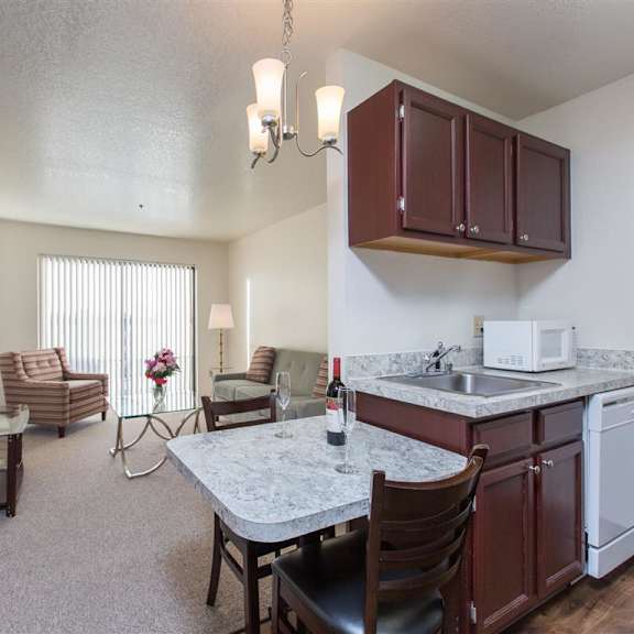 cozy living area here at outlook apartments with striped armchairs, glass table, and flowers. kitchenette has marble countertops and wine. bright, relaxed ambiance.