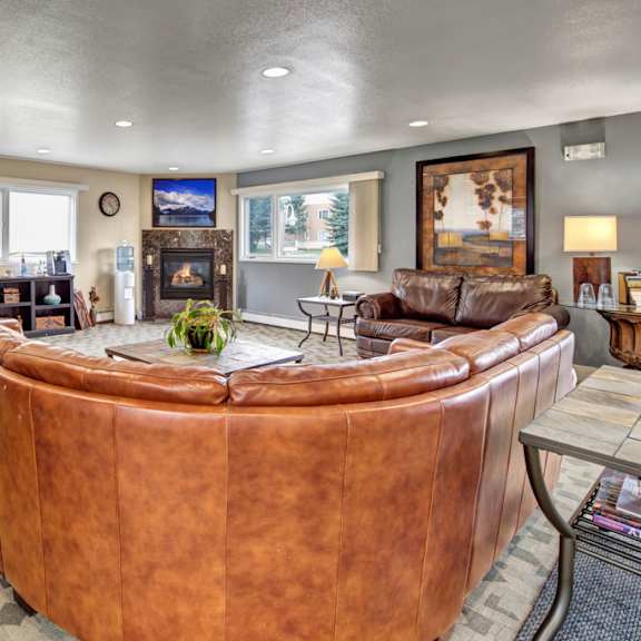 a spacious, inviting community lounge here at club at eagle pointe featuring plush leather sectional seating, a cozy fireplace with a mounted tv, warm accent lighting, large windows for natural light, and tasteful artwork throughout, creating a comfortable gathering space for relaxing, socializing, or enjoying quiet time indoors.