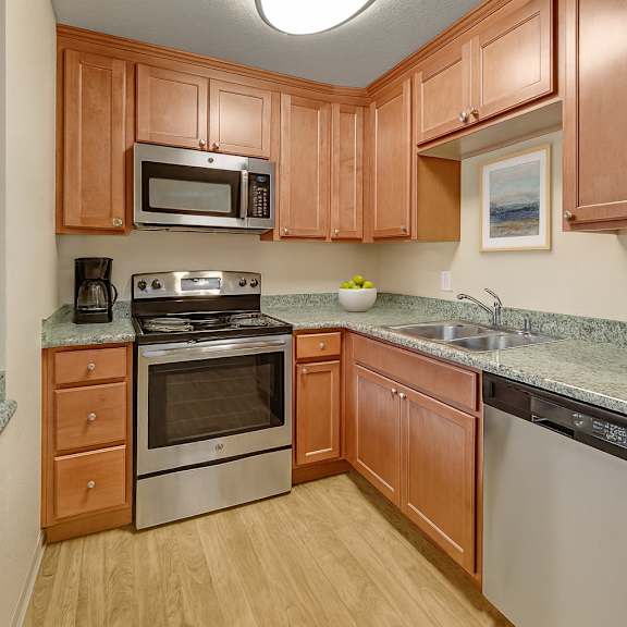 a warm, functional kitchen here at club at eagle pointe featuring natural wood cabinetry, granite-style countertops, and stainless steel appliances including an oven, microwave, and dishwasher. durable wood-style flooring and ample counter space create a practical layout that supports everyday cooking and comfortable meal preparation.