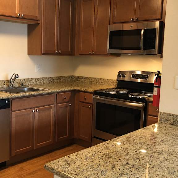 a spacious kitchen here at club at eagle pointe featuring warm wood cabinetry, granite-style countertops, and stainless steel appliances including a refrigerator, range, microwave, and dishwasher. the functional l-shaped layout offers generous counter space, ample storage, and a breakfast bar ideal for meal prep and casual dining.