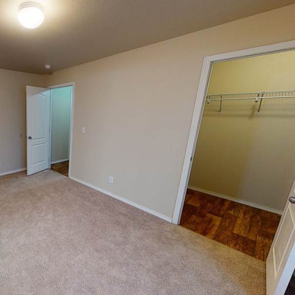 a spacious, carpeted bedroom here at four seasons featuring warm neutral walls, soft overhead lighting, and an open layout that allows for flexible furniture placement. an adjacent walk-in closet provides ample storage, while nearby doorways connect smoothly to the rest of the apartment for added convenience.