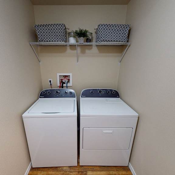 convenient, in-home laundry area here at four seasons featuring a full-size washer and dryer set neatly tucked into a dedicated laundry nook. neutral walls, overhead shelving for storage, and durable flooring create a clean, functional space that makes everyday laundry tasks simple and organized.