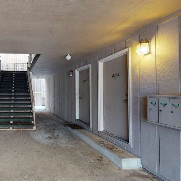 apartment hallway here at rancho tudor apartments with beige walls and closed brown doors numbered 403, 410, 409, 404. central staircase leads to upper floor. lit by small ceiling lights. calm atmosphere.