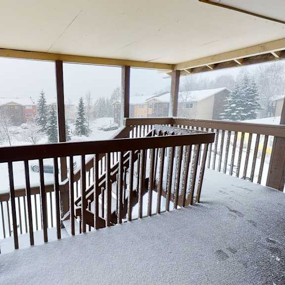 snow-covered porch here at the club at eagle pointe apartments with wooden railings overlooks a snowy neighborhood. fir trees and houses are visible under a gray, overcast sky. quiet, wintry scene.