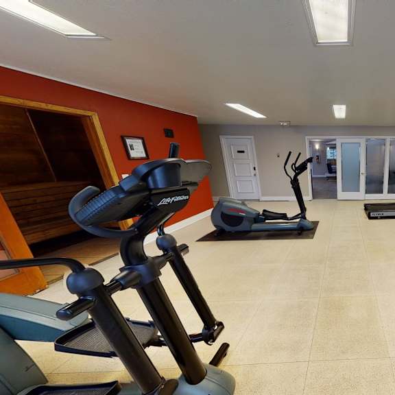 bright gym room here at the club at eagle pointe apartments featuring treadmills, ellipticals, and stationary bikes on tiled floor. mirrors and a flatscreen tv create a modern, spacious feel.