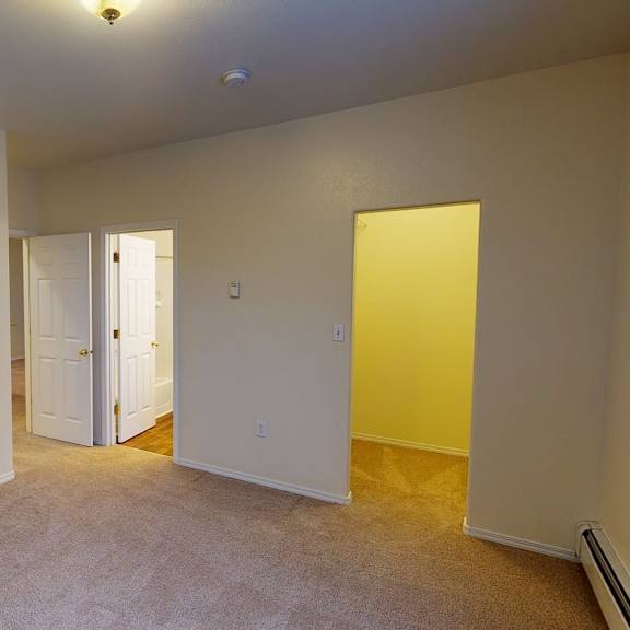 empty bedroom here at the highlands luxury apartments with beige walls and carpet, featuring three open white doors leading to a bathroom and hallway. soft lighting creates a calm atmosphere.