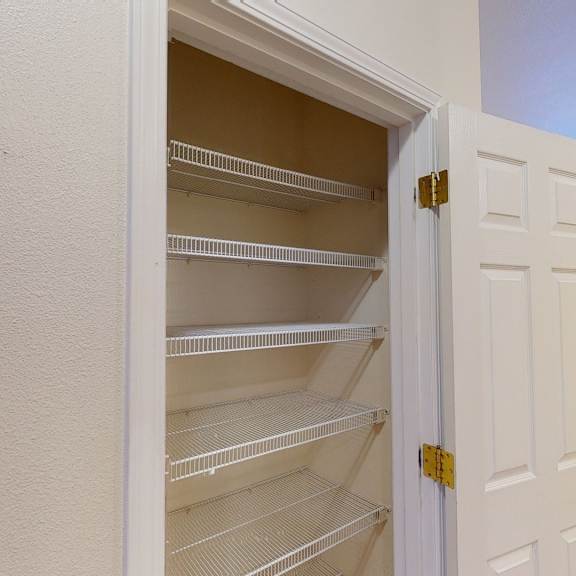 open white closet door revealing empty wire shelves inside a beige wall alcove. bright room here at the highlands luxury apartments with carpet and window in the background.