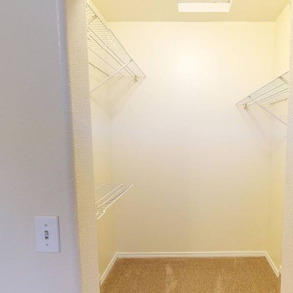 walk-in closet here at the highlands luxury apartments with beige walls, carpeted floor, and wire shelving on three sides. a single ceiling light provides a bright, clean ambiance.