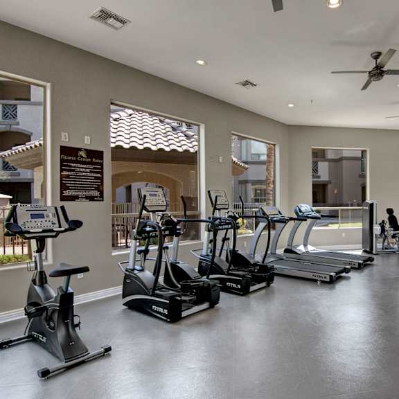 a spacious fitness center here at sonoma landing featuring rows of treadmills and elliptical machines, a stationary bike, and strength training equipment arranged on sleek flooring, with large windows bringing in natural light, neutral walls, ceiling fans, recessed lighting, and views of the surrounding apartment community.