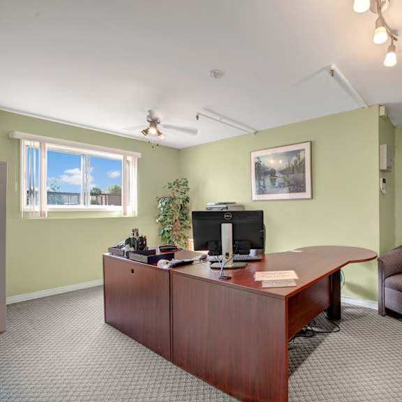 a welcoming on-site office here at gateway square with soft green walls, a large wooden desk, comfortable seating, framed artwork, and bright lighting creating a professional and inviting atmosphere.
