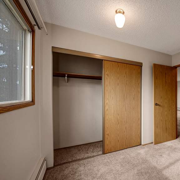 a bright, empty bedroom here at gateway square featuring soft neutral walls, plush carpet flooring, and a large window with warm wood trim, plus a spacious sliding-door closet and an open layout that feels clean and comfortable.