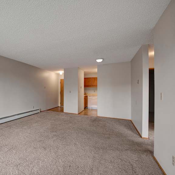 a bright open living space here at gateway square featuring soft neutral walls, plush carpet flooring, and a long layout that offers plenty of room to relax, with a cozy flow leading into the kitchen area for easy everyday living.