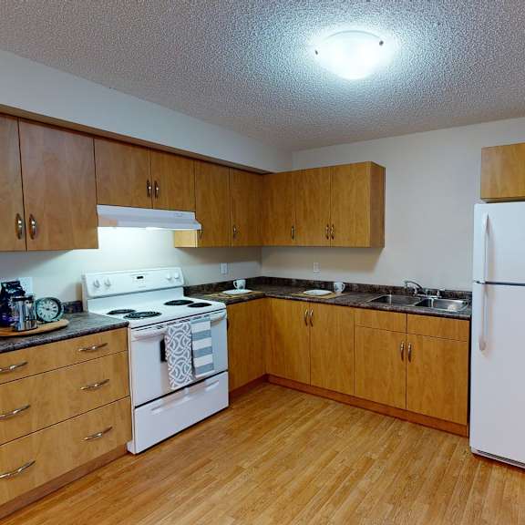 a bright, spacious kitchen here at sonora featuring warm wood cabinetry, durable laminate countertops, white appliances including a full-size refrigerator and electric range, wood-style flooring, generous counter space, and an open layout that offers easy access to the adjoining hallway and living areas.